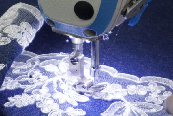 A close-up shot of a sewing machine with a fine needle working on delicate lace lingerie.