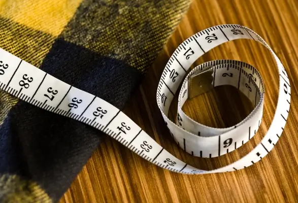 An inspector measuring a bra's band size on a flat table with a measuring tape.