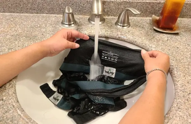 A person gently hand-washing a sports bra in a sink with cold water.
